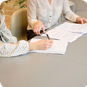 Two people sitting at a table with papers and pens.